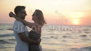 在靠近海洋的日落时，有魅力的情侣拥抱。 蜜月度假概念。